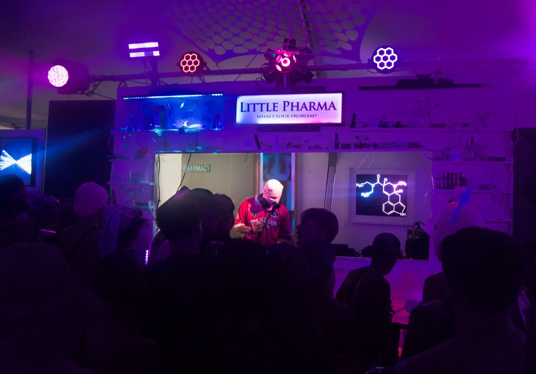 DJ performing under purple lights in the pharmacy-themed Little Pharma stage with neon molecule graphics