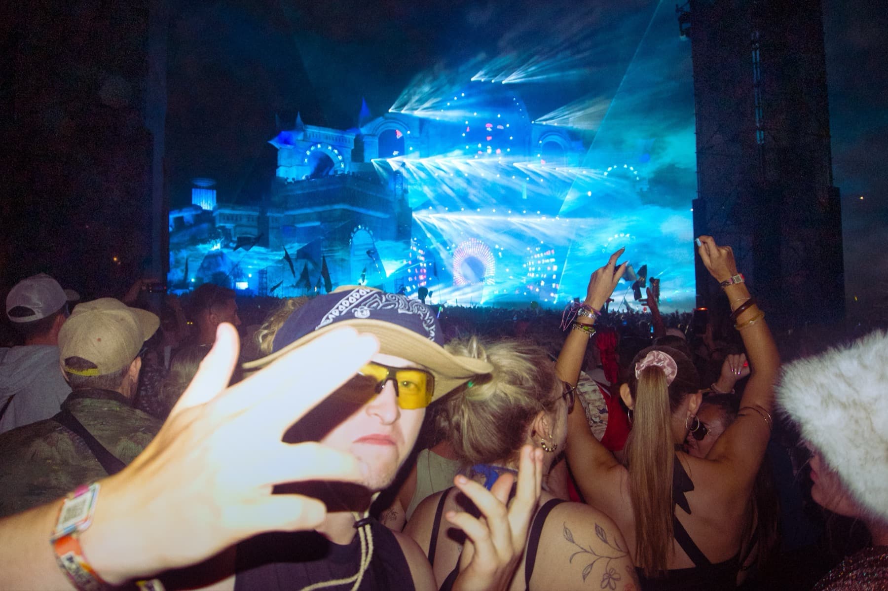 Reveller in a cowboy hat reaching toward the camera with blue stage lights illuminating the crowd behind