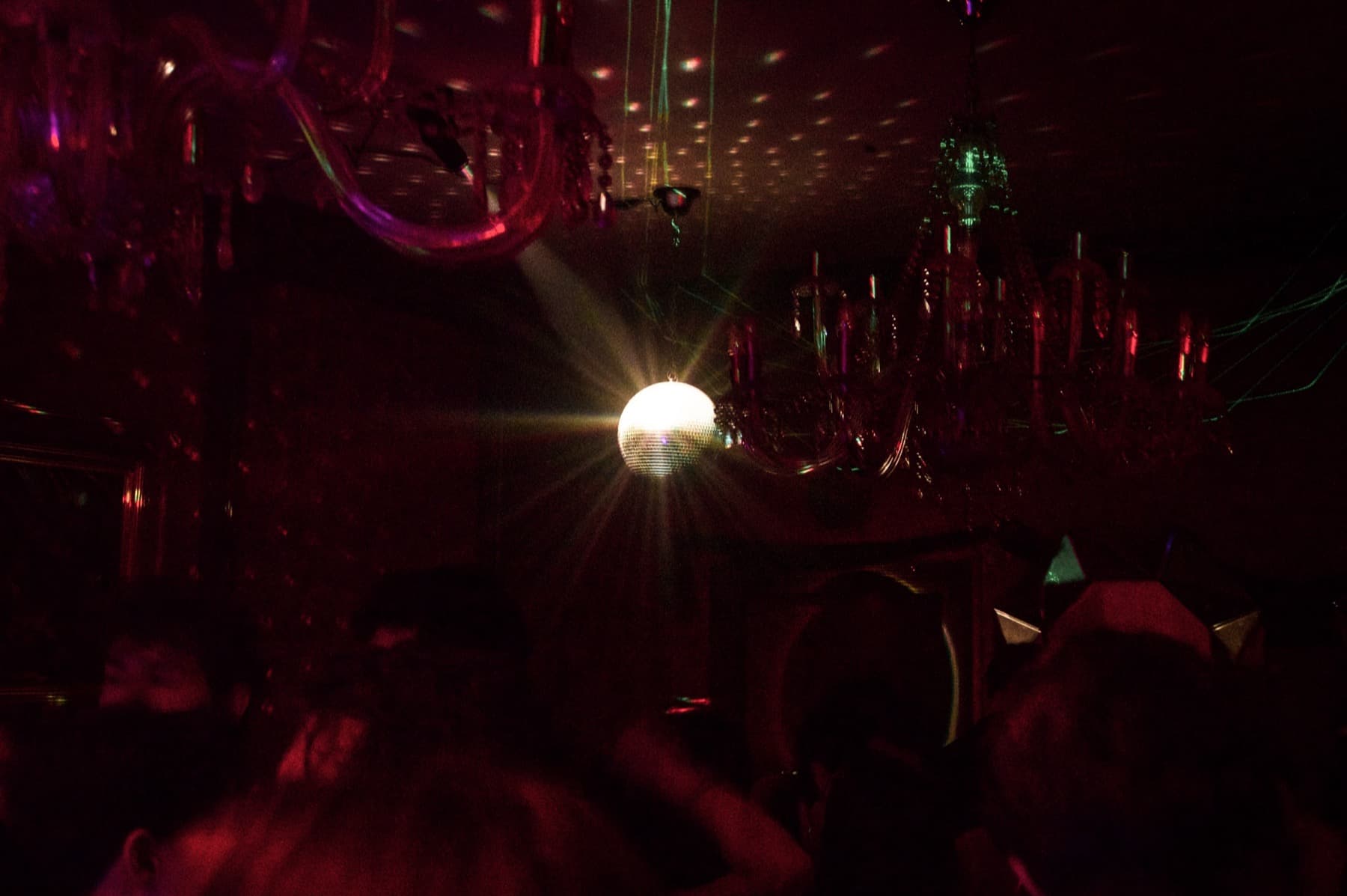 Glowing mirror ball casting light through a dark room filled with chandeliers and red-purple haze