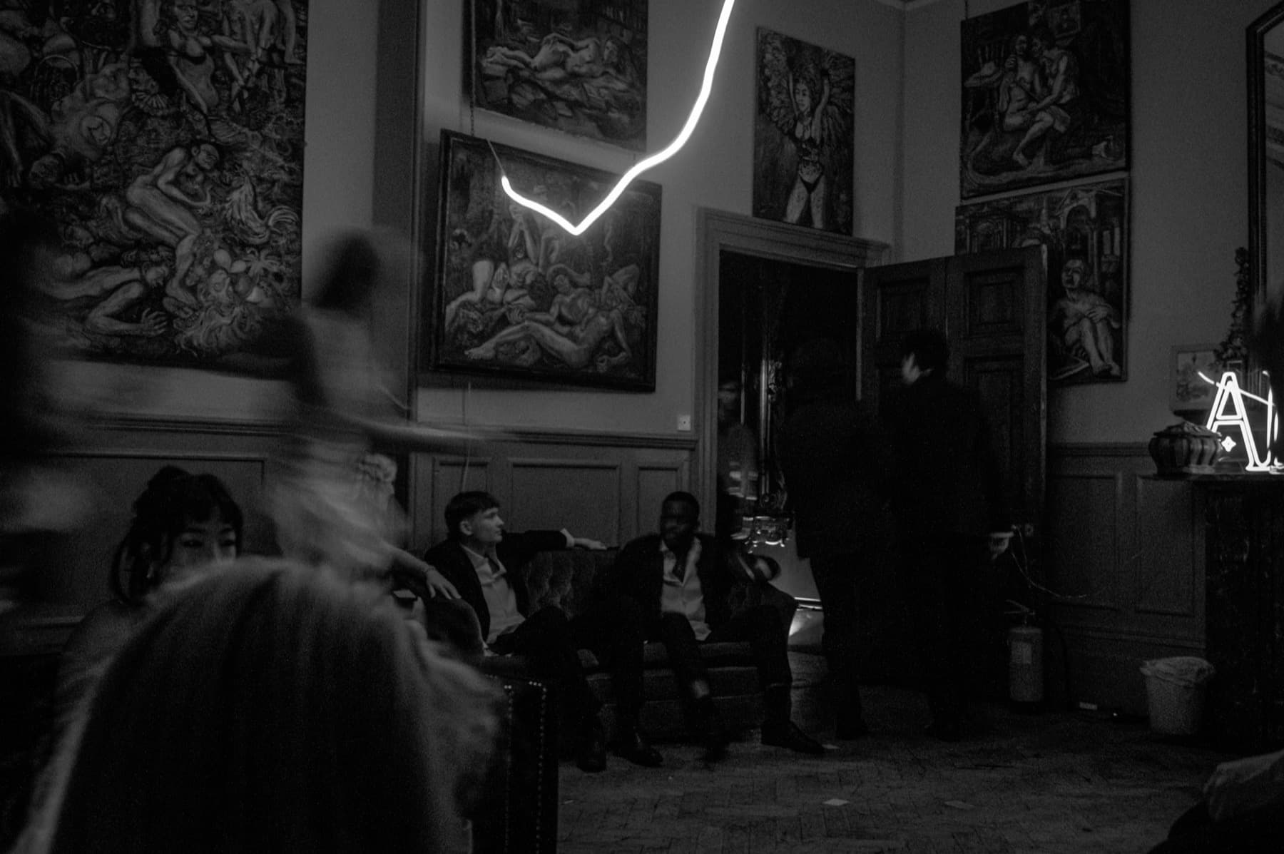 Guests lounging on sofas beneath large oil paintings and a neon light installation in a grand room