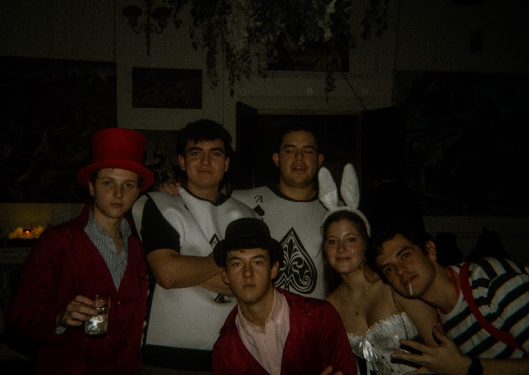 Group in Wonderland-themed costumes including a red top hat, ace of spades shirt, and bunny ears posing together