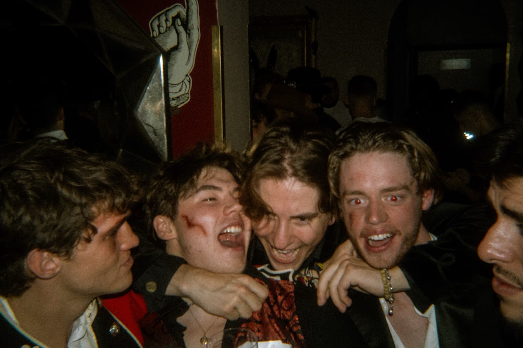 Group of friends laughing and grabbing each other with fake blood makeup in a dark party room