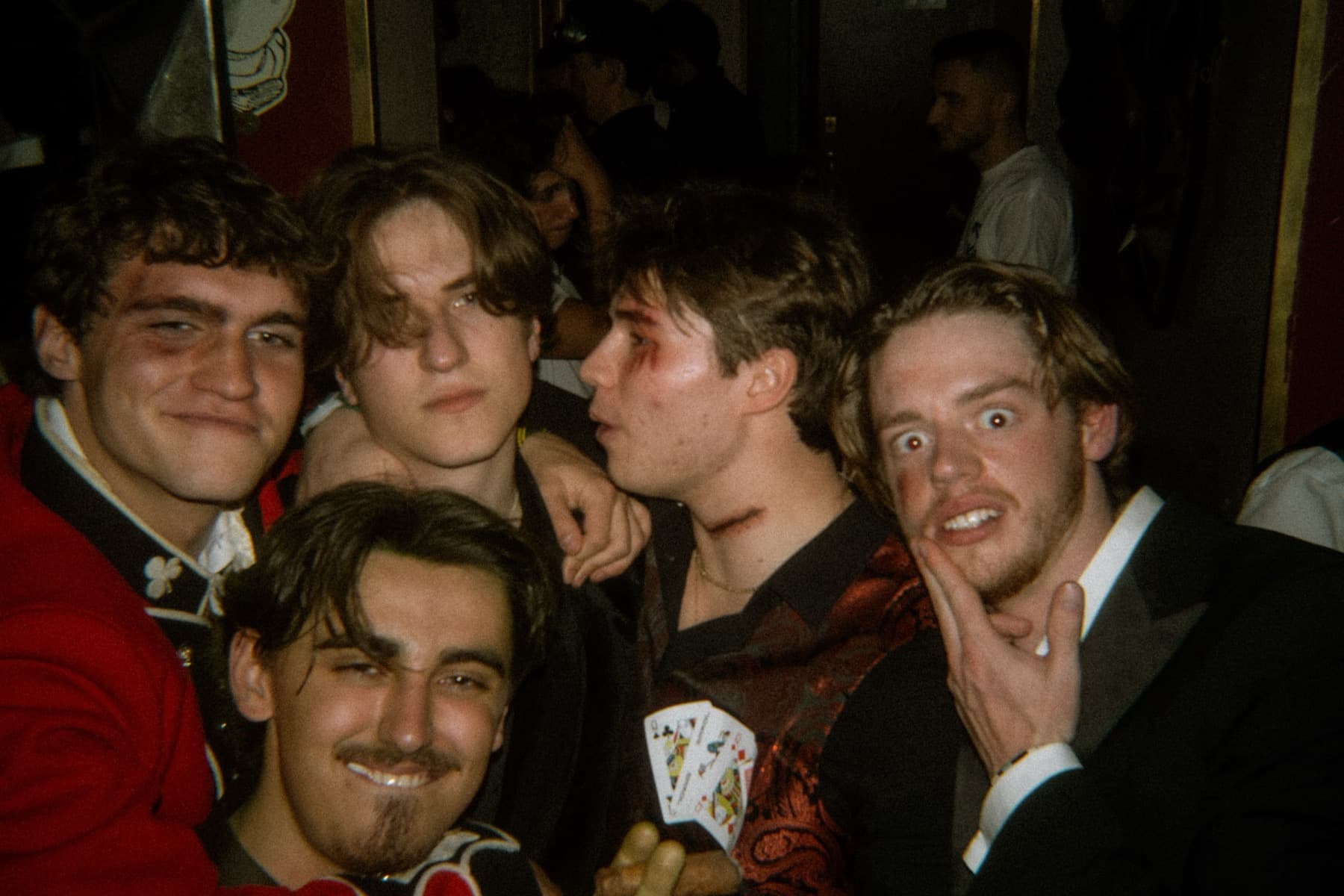 Five friends in costume makeup and formal wear huddled together holding playing cards