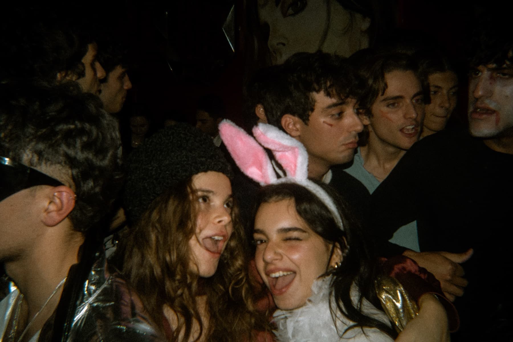 Partygoers in bunny ears and costumes laughing in a tightly packed crowd with Halloween makeup