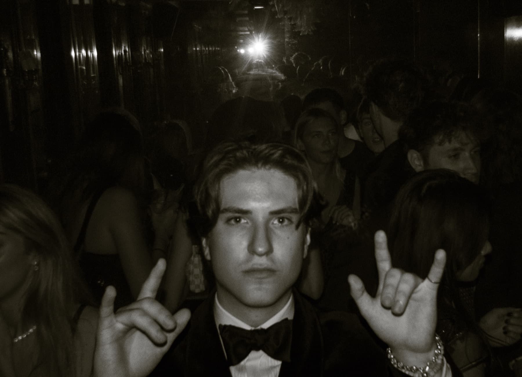 Guest in a bow tie throwing rock-and-roll hand signs in a sepia-toned crowded club