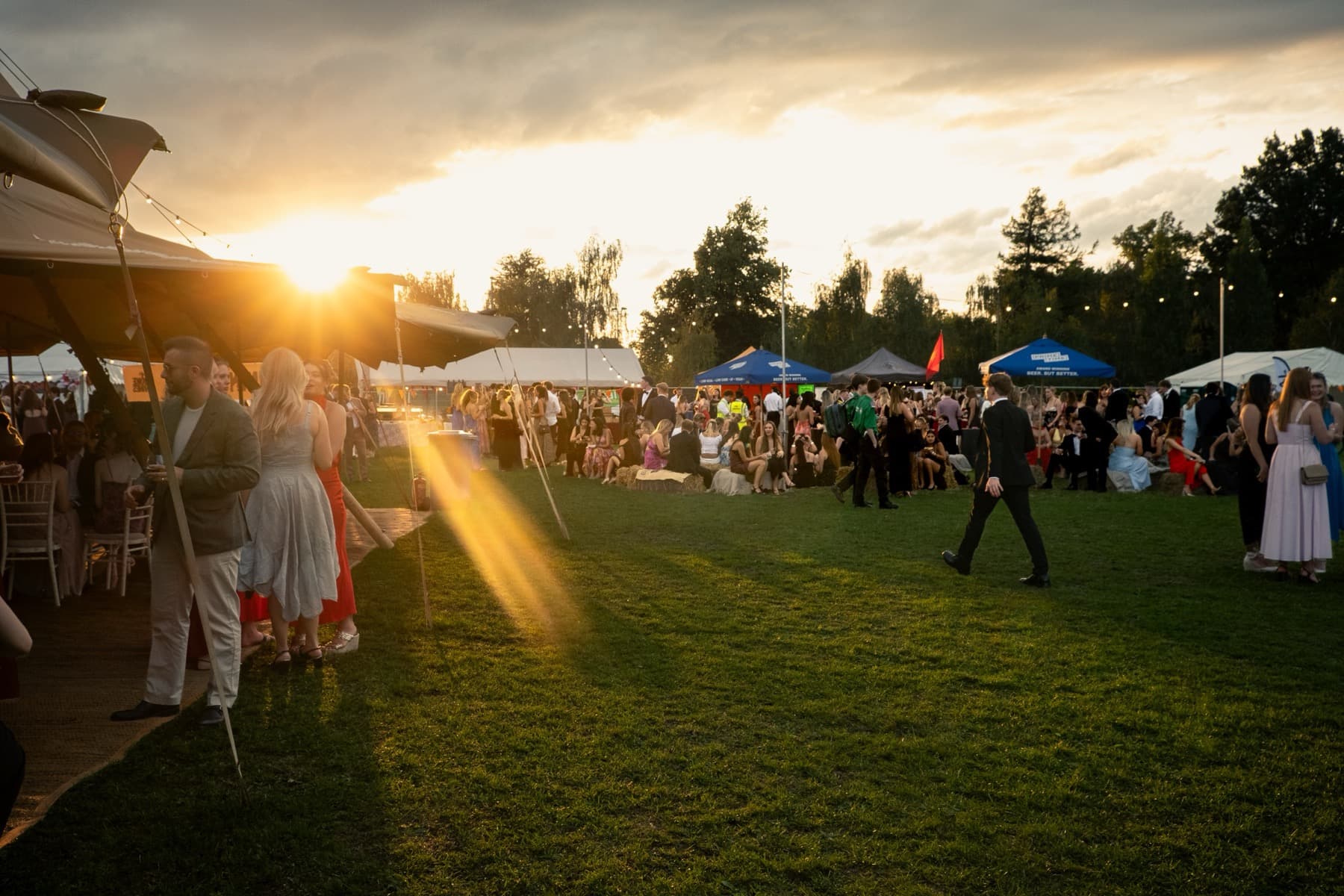 Golden sunset casting long shadows over smartly dressed guests socialising between marquees on the lawn