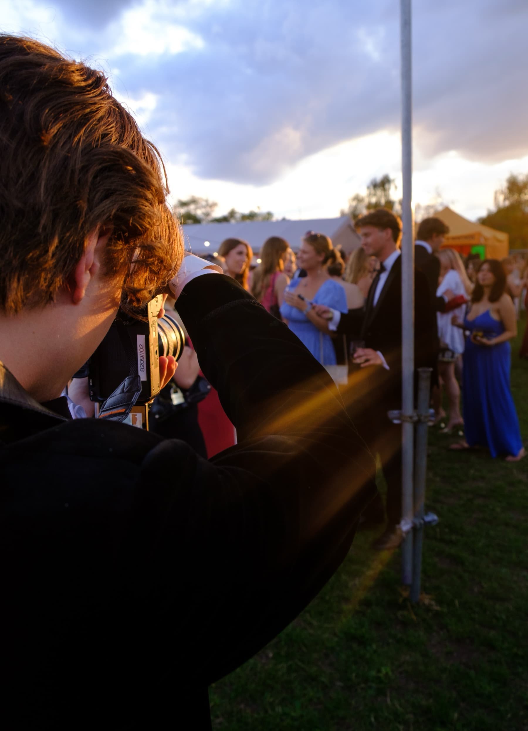Photographer shooting through a film camera with guests in formal wear and a dramatic sunset behind