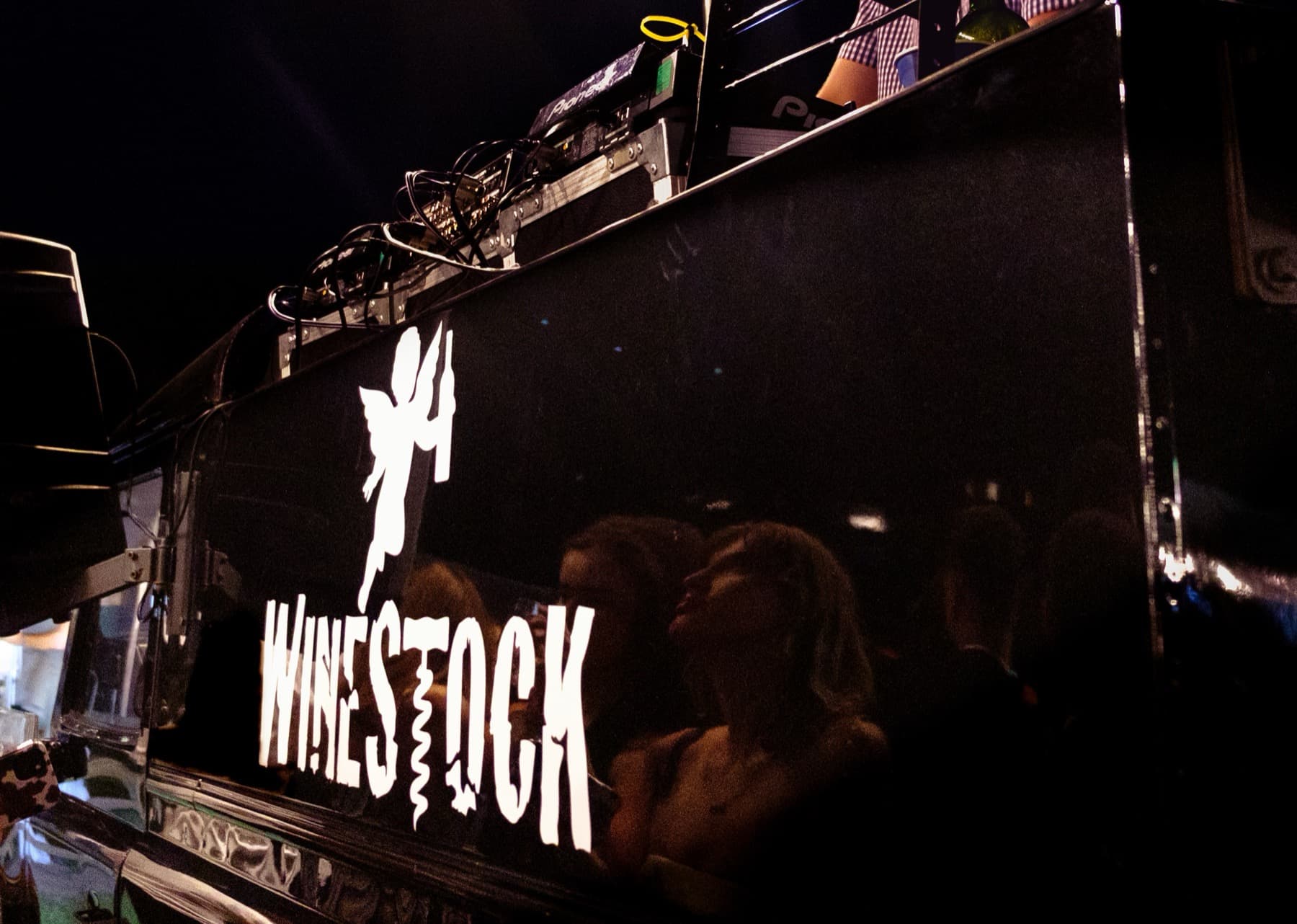 Close-up of the Winestock logo on a glossy black DJ booth reflecting the crowd at night