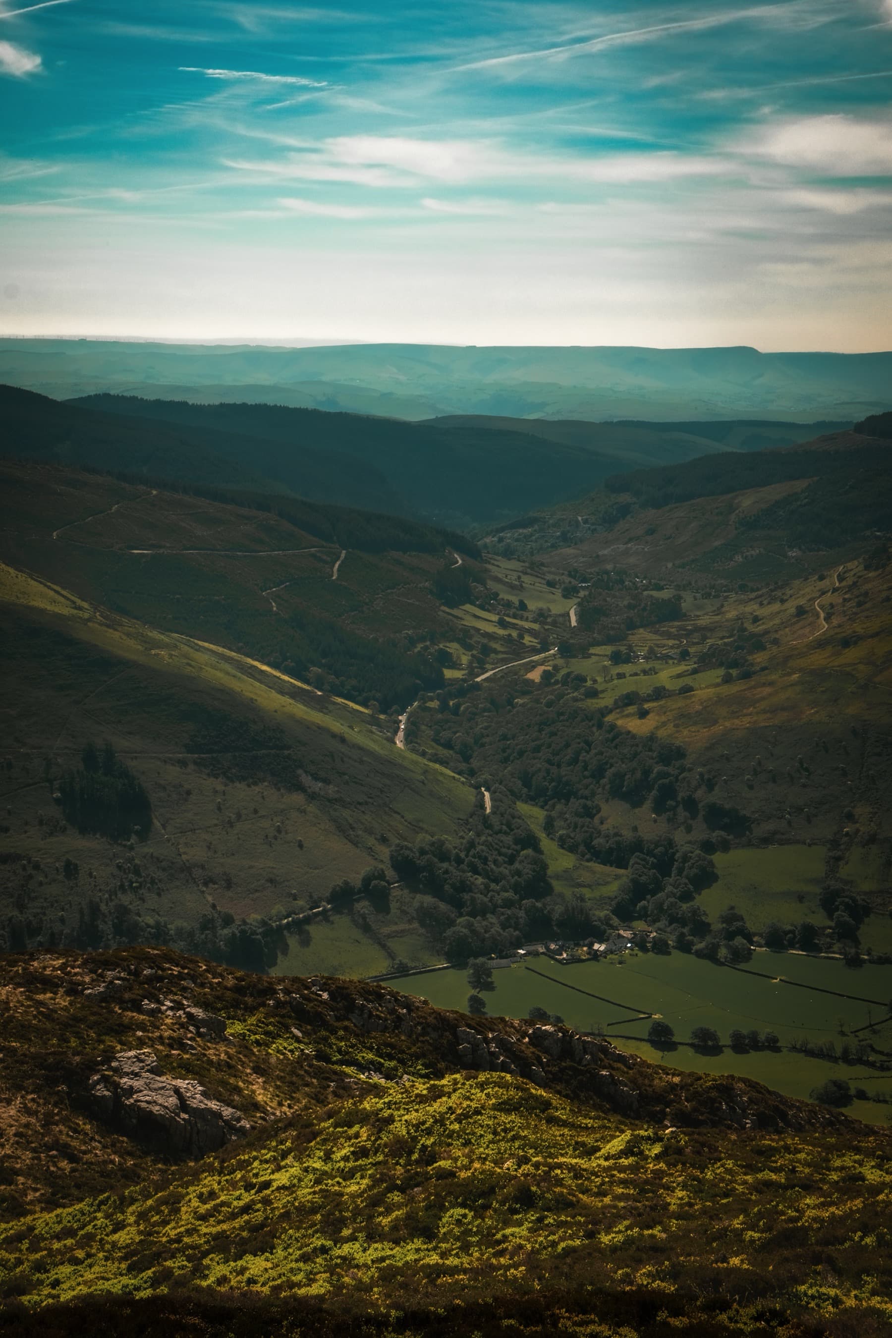Sunlit green valley with a winding road viewed from a high mountain vantage point above the treeline