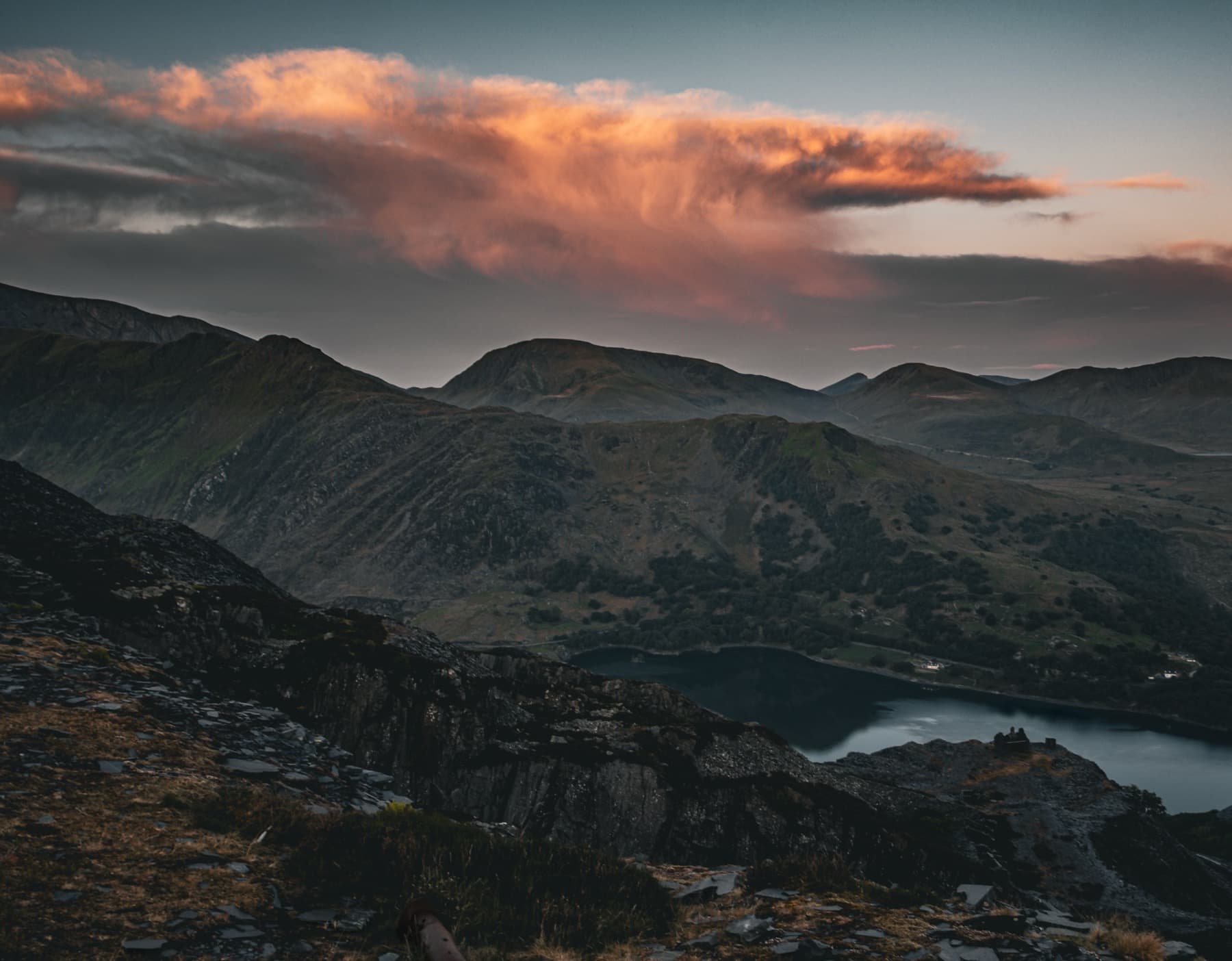 Sunset over Snowdonia mountains with pink and orange clouds reflected in a dark lake seen from the quarry
