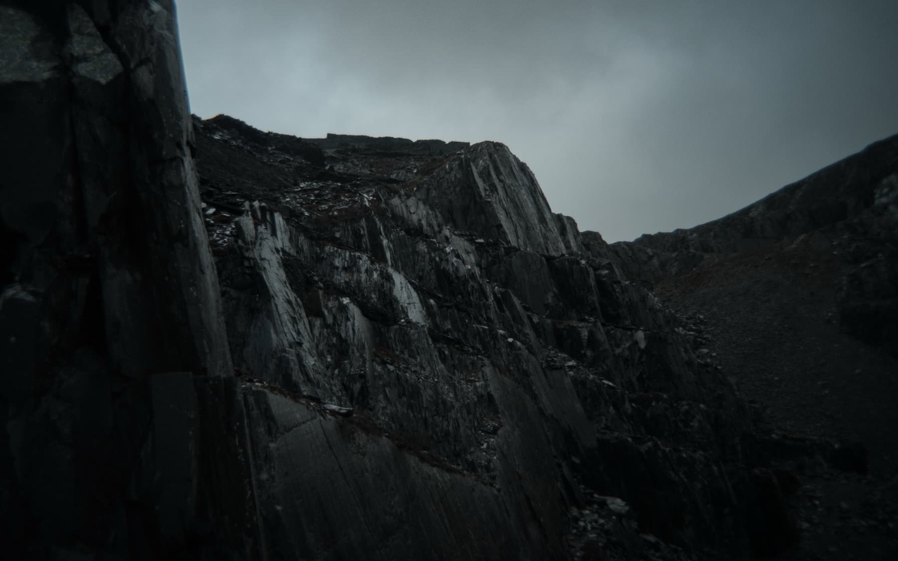 Sheer vertical slate quarry cliff face rising against an overcast grey sky