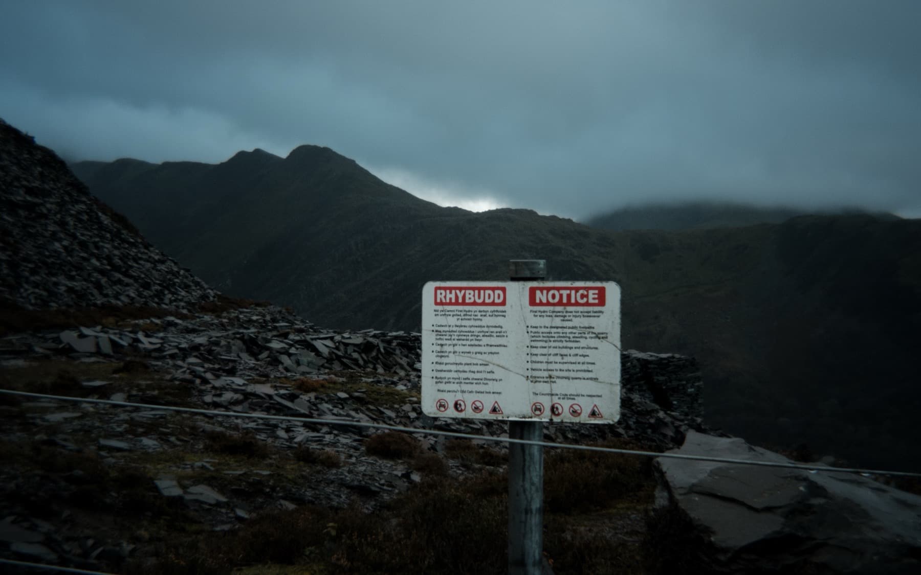Bilingual Welsh and English warning notice sign at the entrance to the quarry with misty mountains behind
