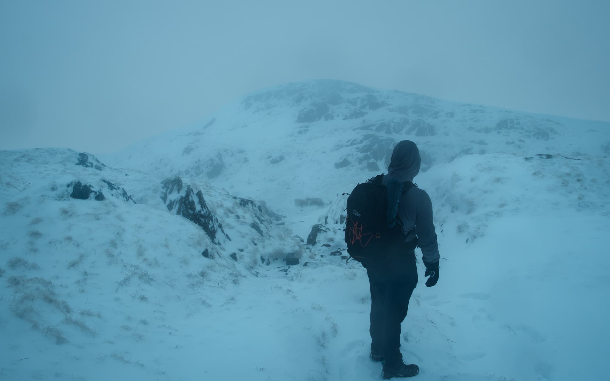 Hiker ascending a snow-covered mountain slope into heavy mist with a backpack and winter gear