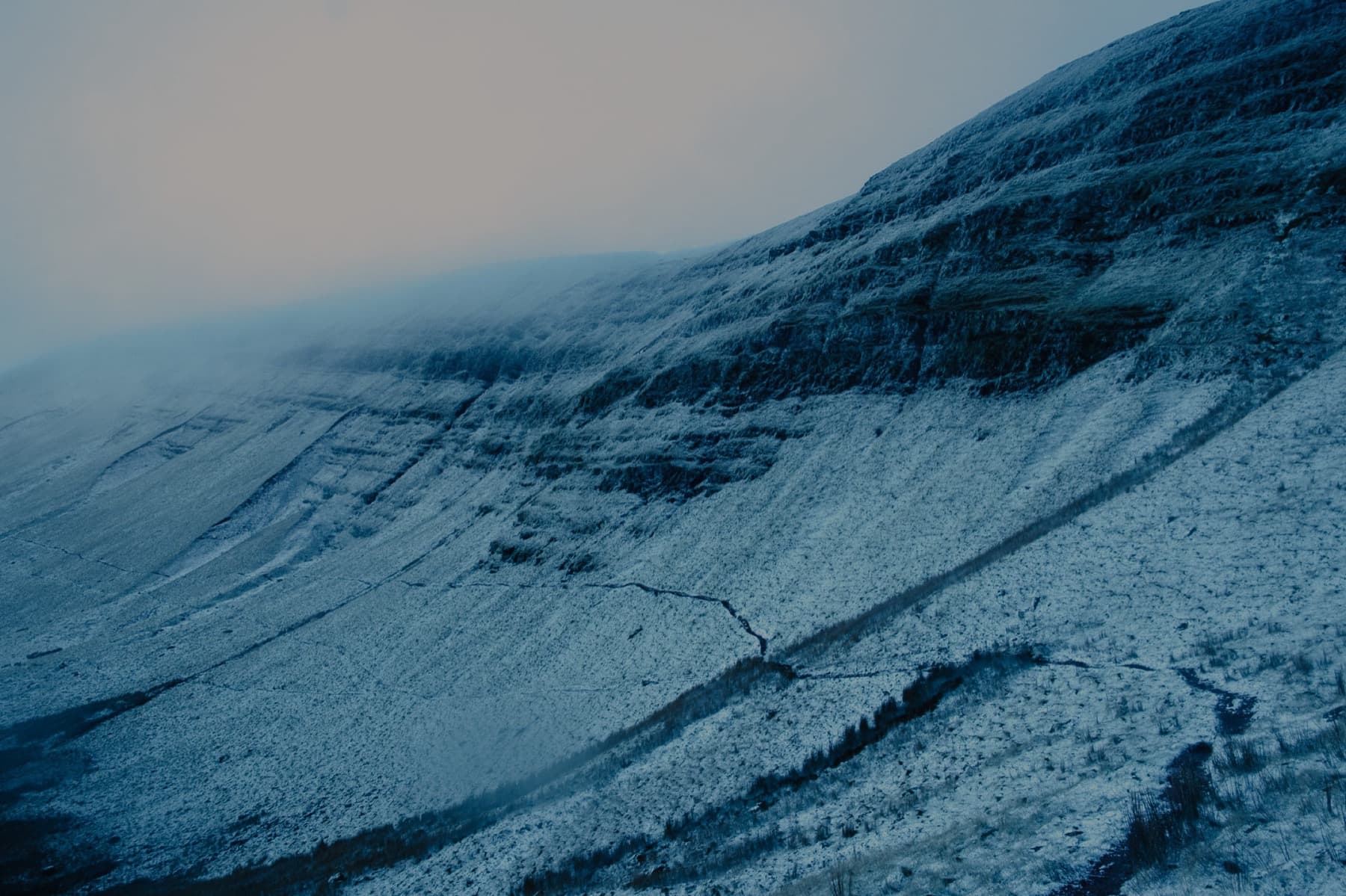 Snow-dusted steep mountainside with exposed rock bands vanishing into low cloud