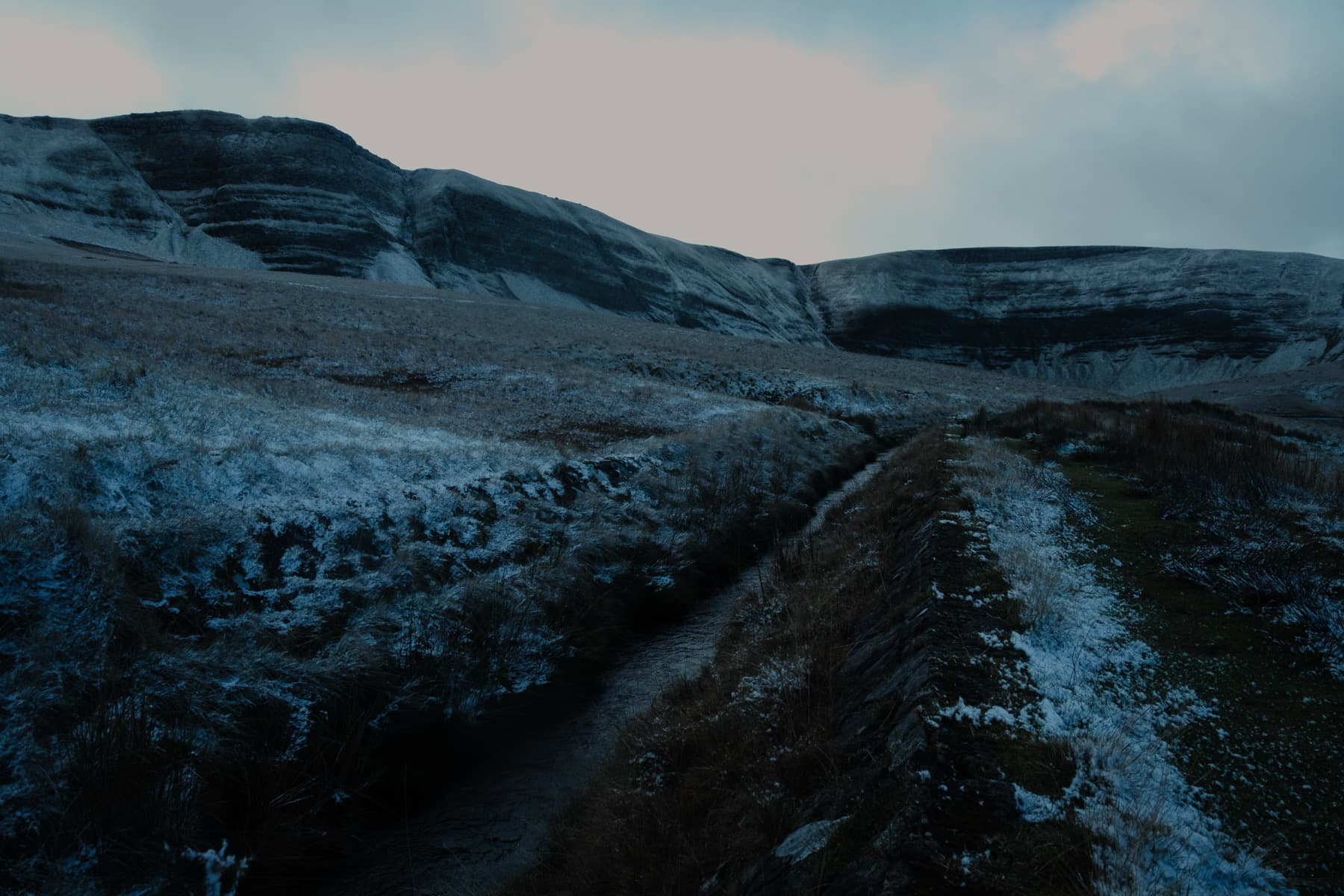 Frosty path leading through moorland toward a snow-dusted escarpment at dusk