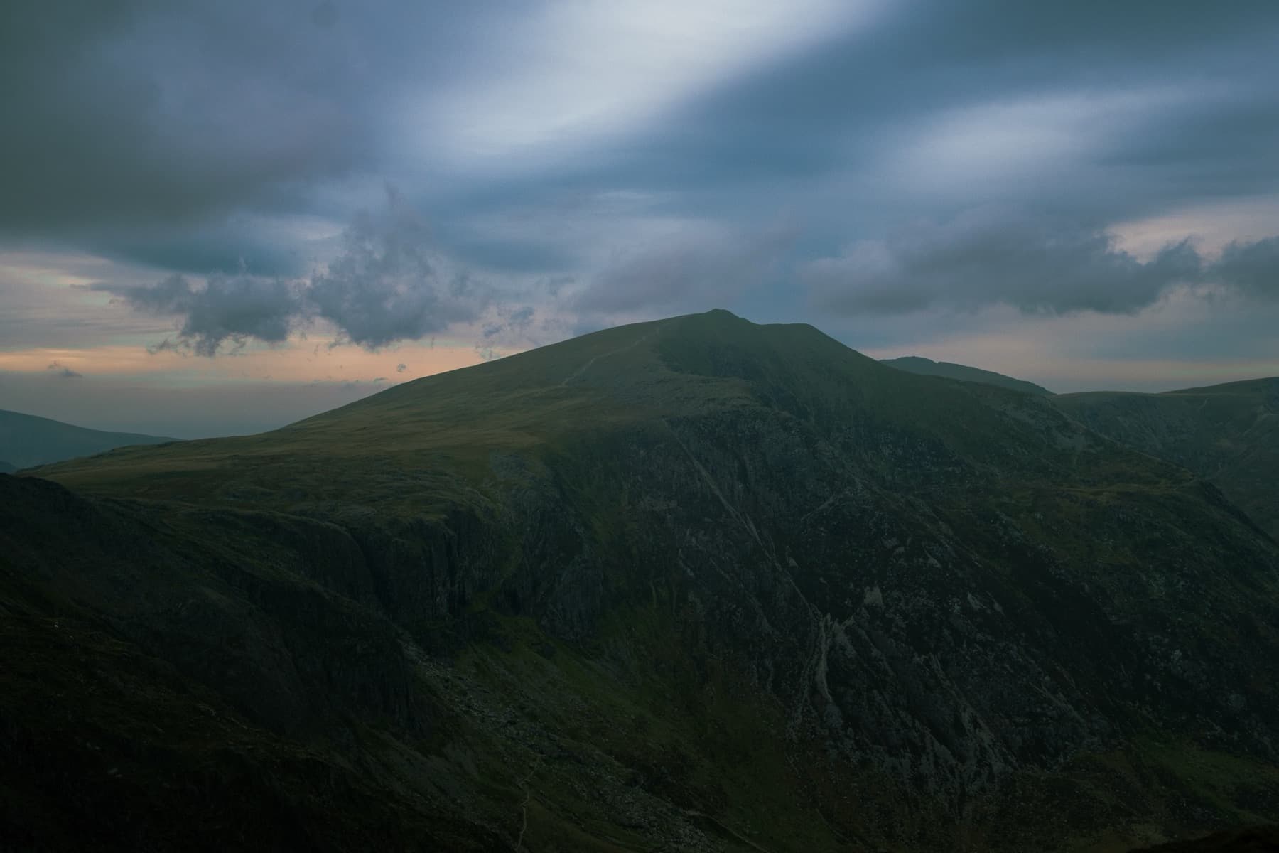 Mountain summit rising against dramatic streaked clouds at dusk with steep gullies falling into shadow