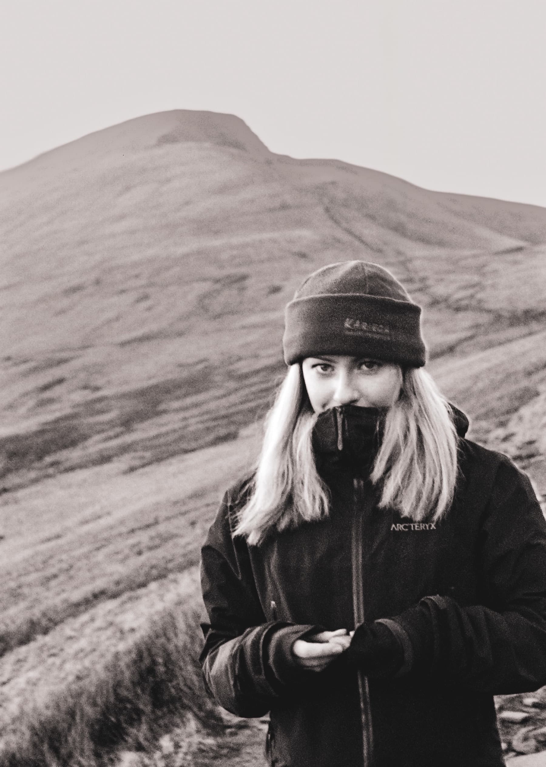 Portrait of a hiker in a beanie and jacket with Pen y Fan rising behind in black and white film