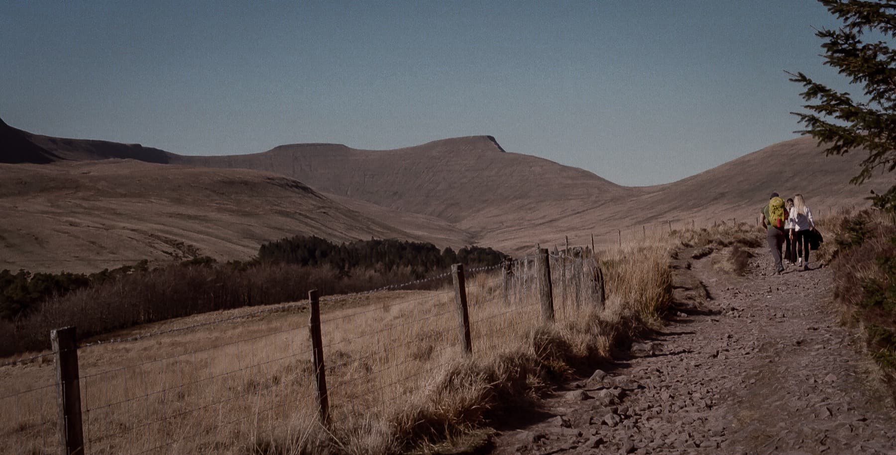 Hikers walking along a fenced track toward Pen y Fan with the flat summit visible in the distance, shot on film
