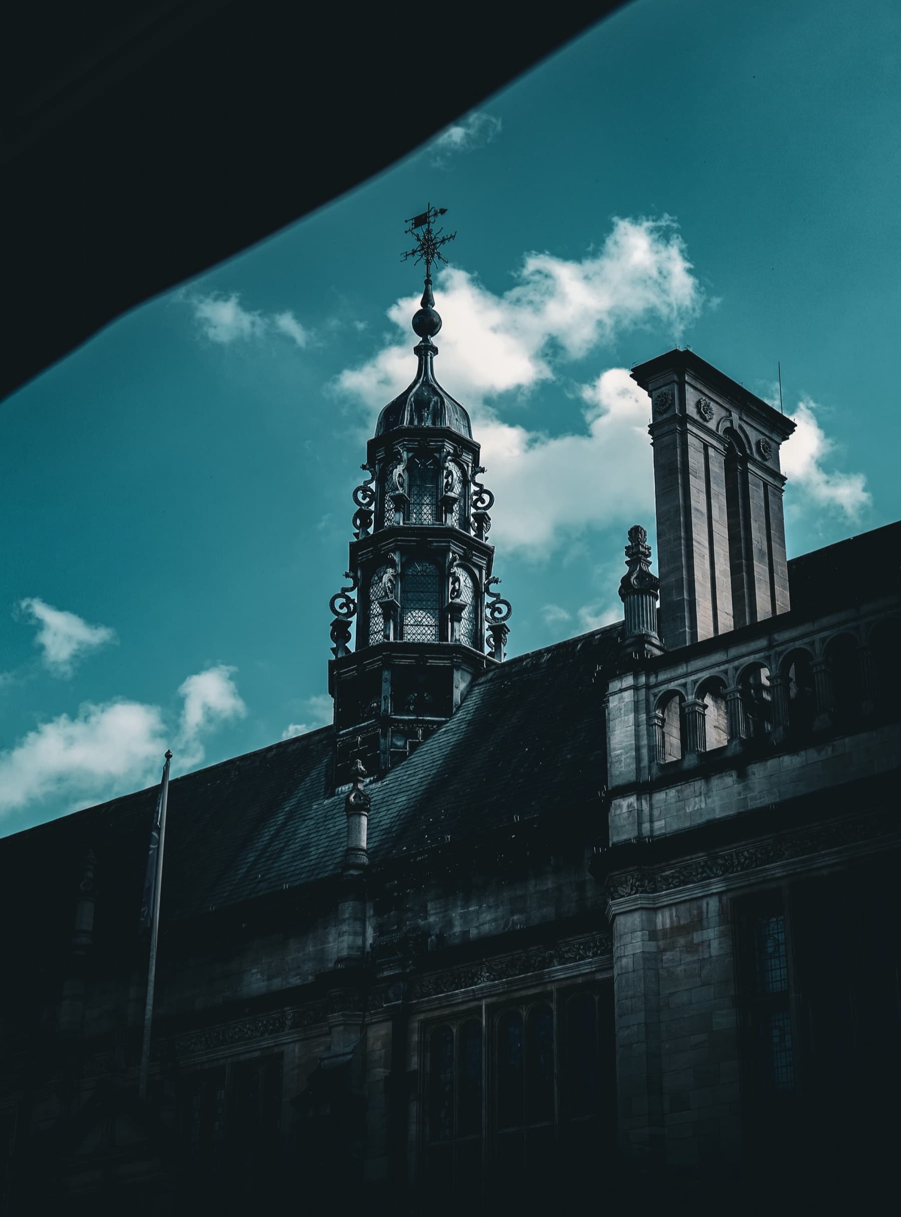 Ornate Gothic turret and weather vane of an Oxford college building shot from below with deep teal sky