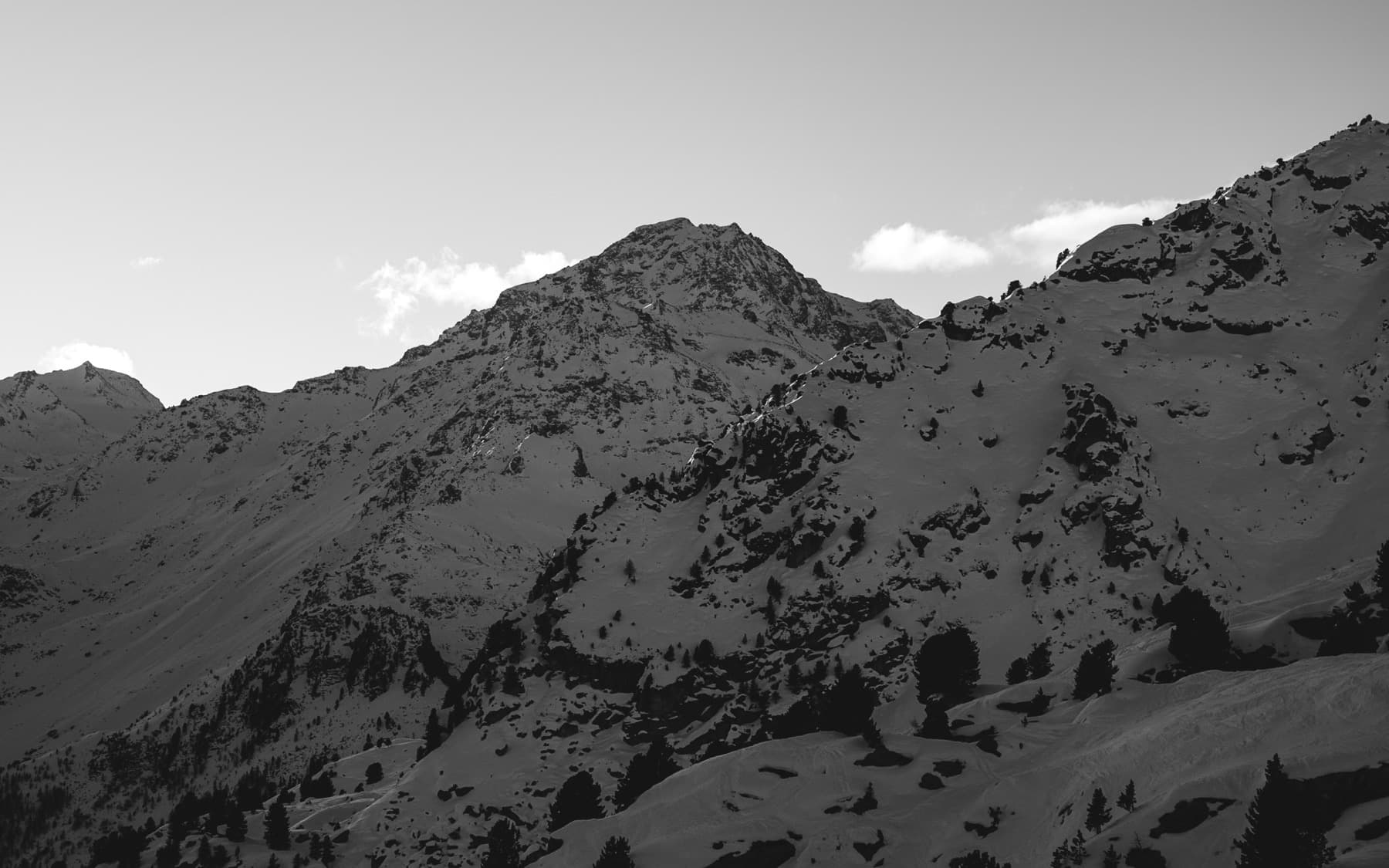 Rugged alpine peak with steep rocky faces and sparse snow cover rising dramatically against a clear sky, shot in black and white