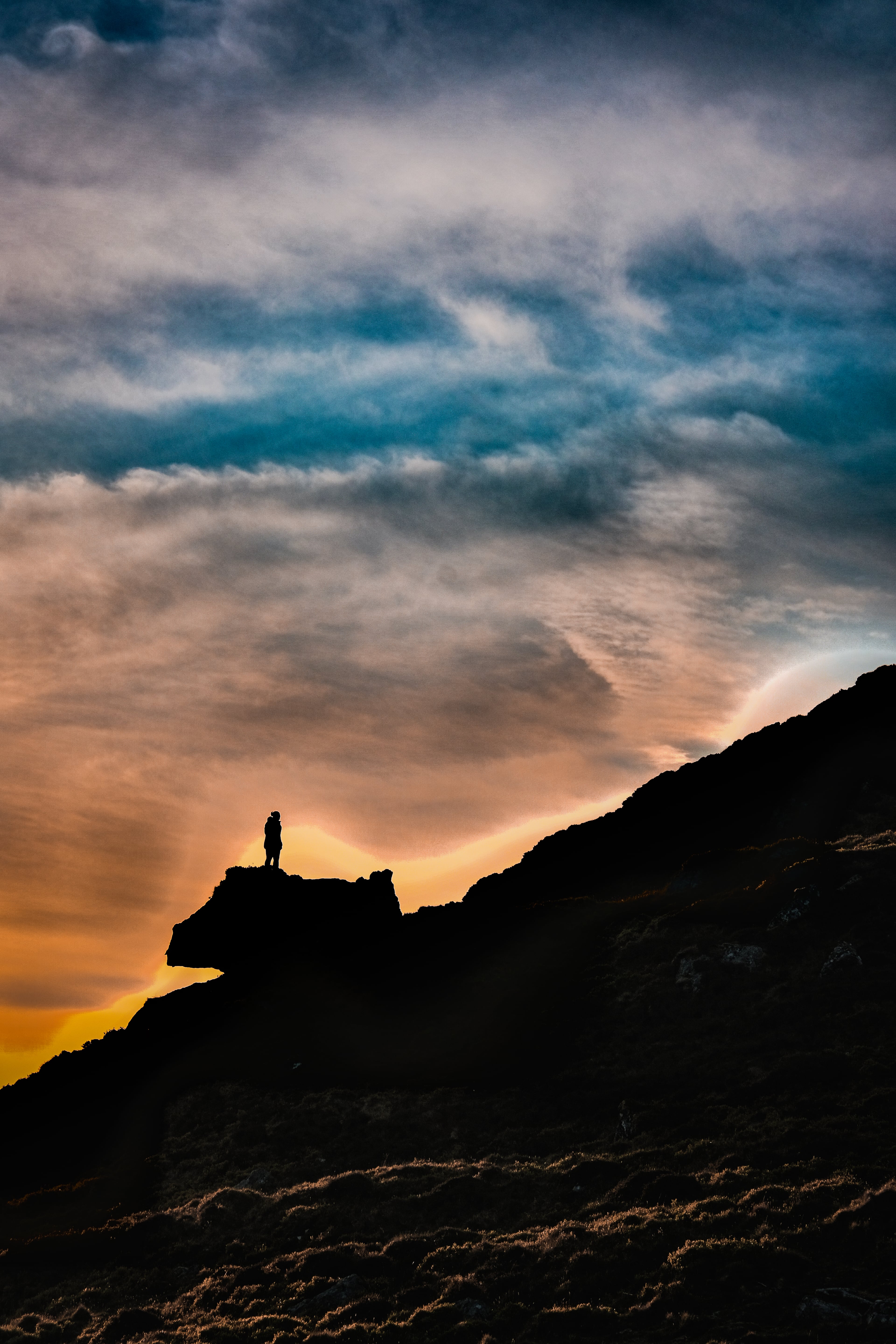 Silhouette of a person standing on a rock outcrop against a dramatic sunset sky
